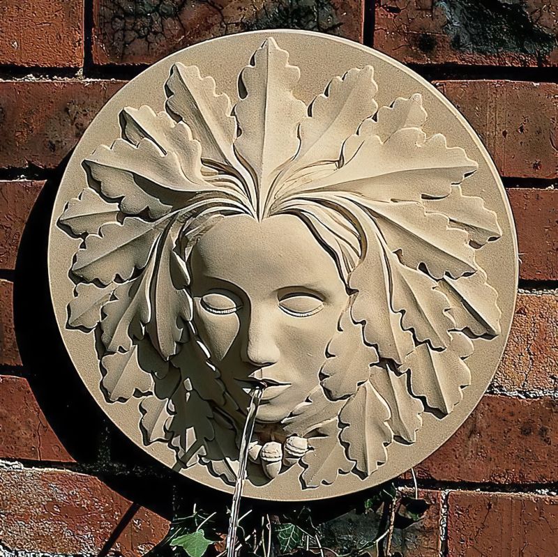 Fontana da parete in pietra a forma di volto con foglie, acqua che scorre dalla bocca su un muro di mattoni