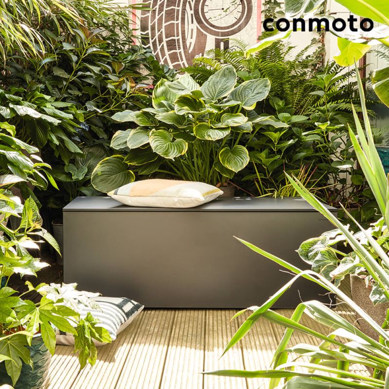 Boîte noire moderne en métal comme décoration de jardin, entourée de feuillage vert sur une terrasse en bois