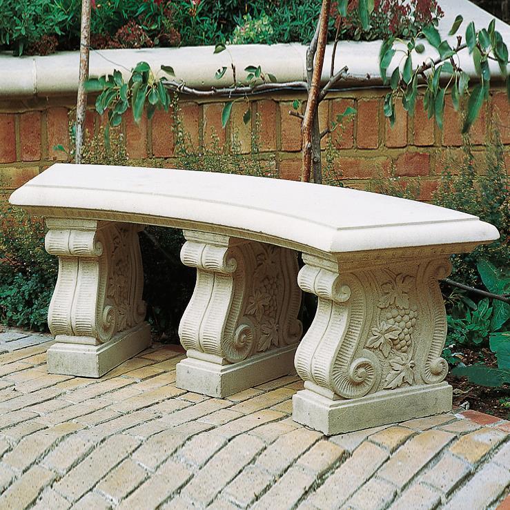 Panca da giardino beige in pietra con tre colonne decorate come gambe su pavimentazione in pietra