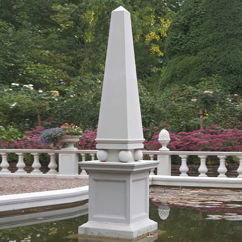 Obélisque blanc moderne avec ornements en boule dans un étang de jardin devant un arrière-plan vert
