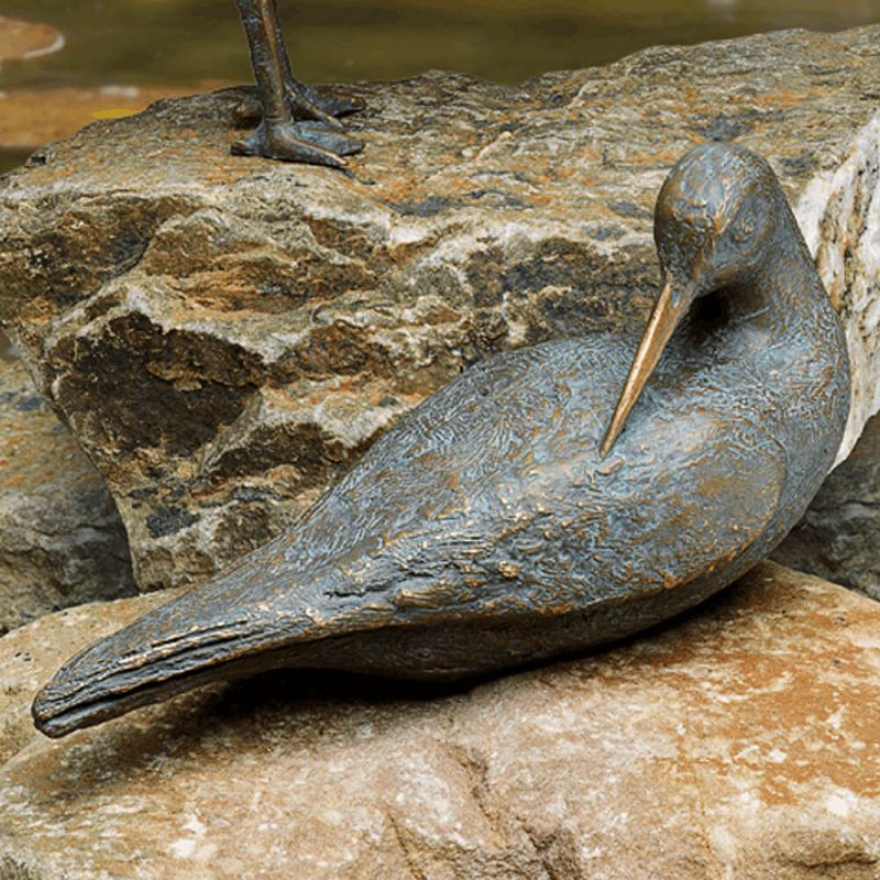 Photo rapprochée d'une sculpture d'oiseau en métal posée sur une pierre en décoration de jardin