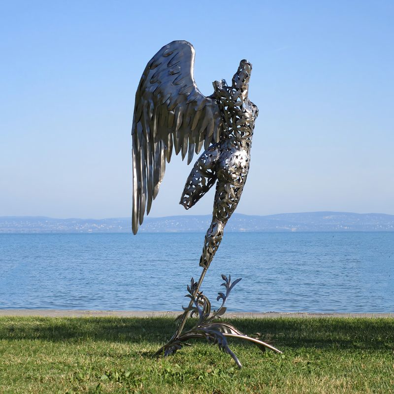 Figure d'ange en métal aux ailes déployées sur pelouse devant un lac