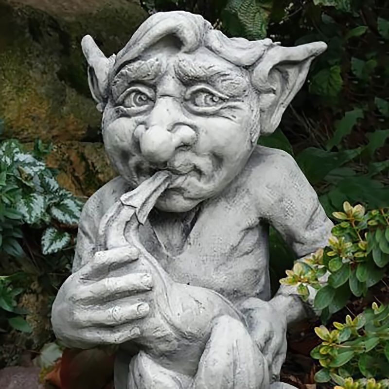 Sculpture de gobelin en pierre avec une pipe dans un jardin parmi les plantes