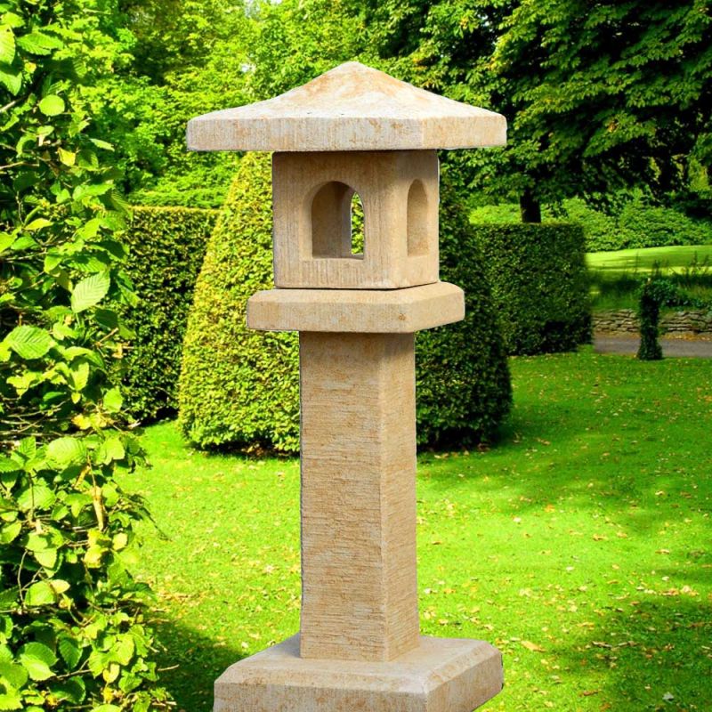 Lanterne de jardin beige en pierre devant des buissons verts sur une pelouse bien entretenue
