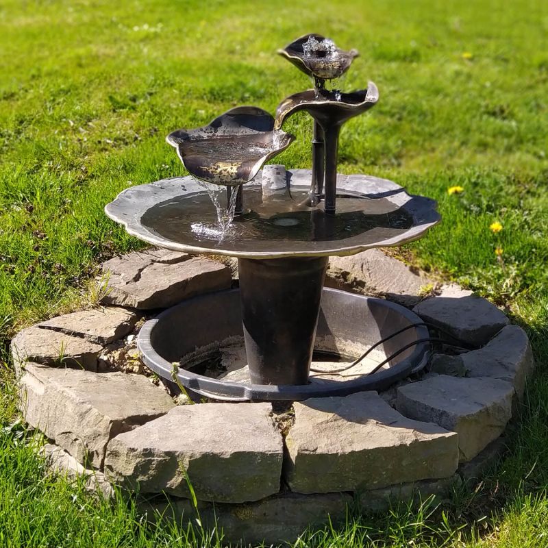 Fontaine de jardin noire avec deux oiseaux sur un muret décoratif en pierre dans la pelouse verte