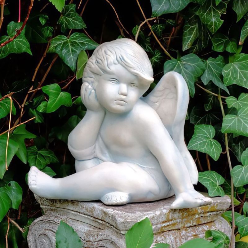 Figure d'ange blanche assise sur une pierre entourée de lierre vert