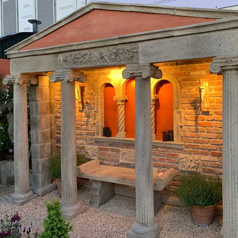 Casetta da giardino in pietra con colonne, panchina e luce calda al crepuscolo
