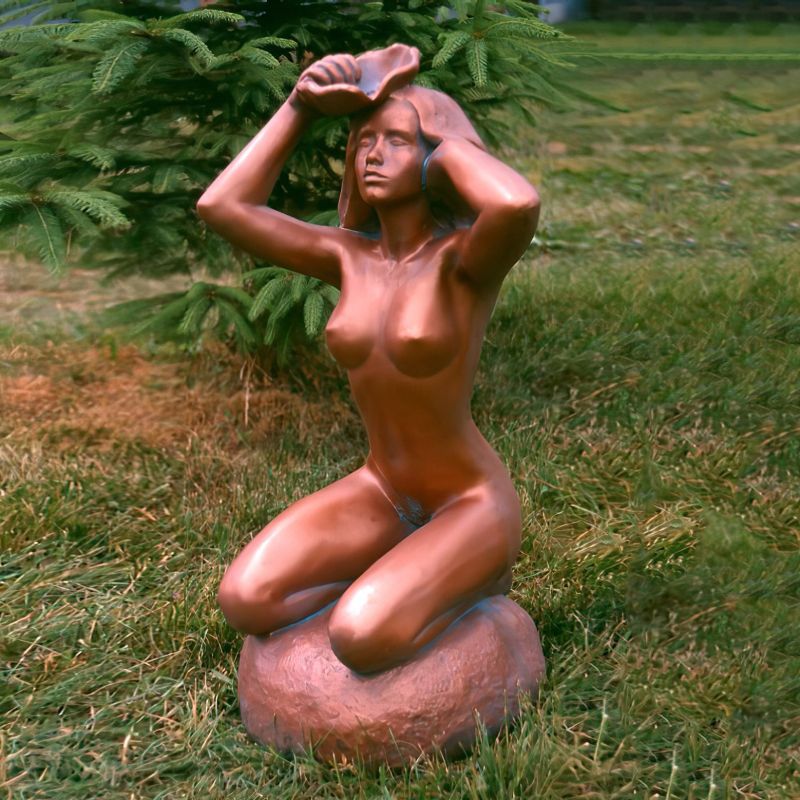 Statua in bronzo di una donna nuda inginocchiata su una pietra nel giardino, circondata da erba e alberi