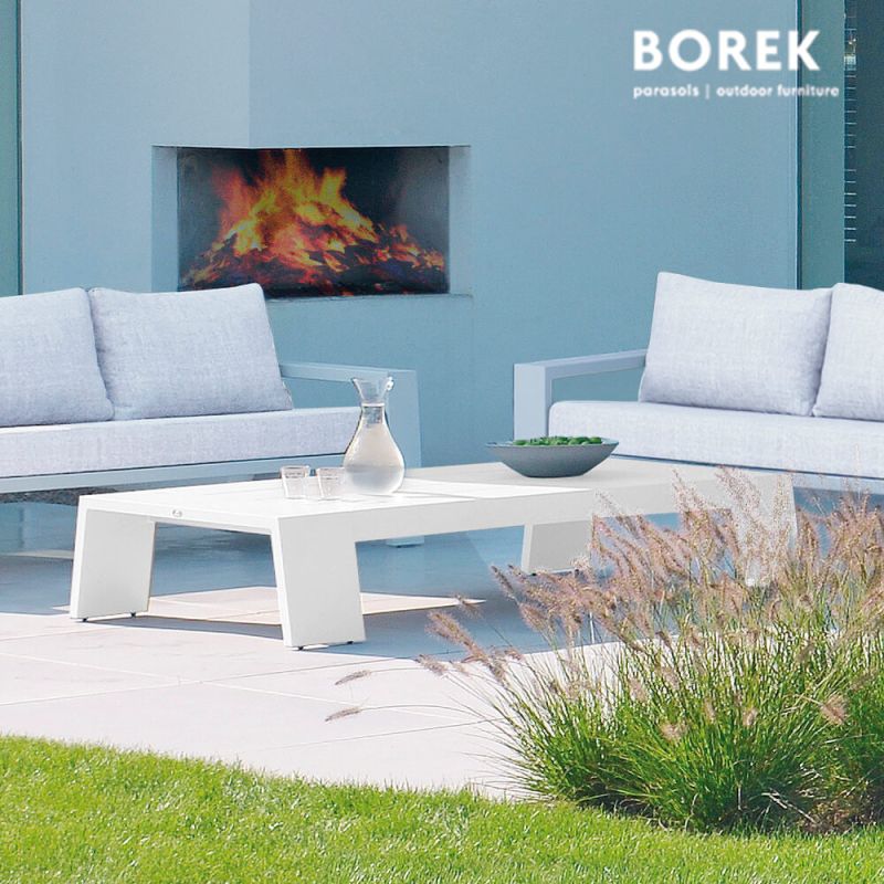 Canapé de jardin blanc moderne et table basse devant une cheminée encastrée avec flammes