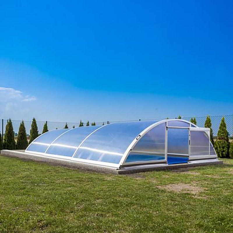 Couverture de piscine transparente et arrondie sur pelouse verte sous un ciel bleu