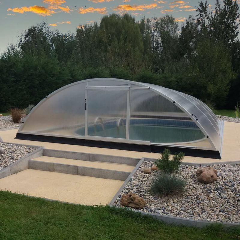 Abri de piscine transparent et arrondi dans un jardin avec des parterres de gravier et une pelouse