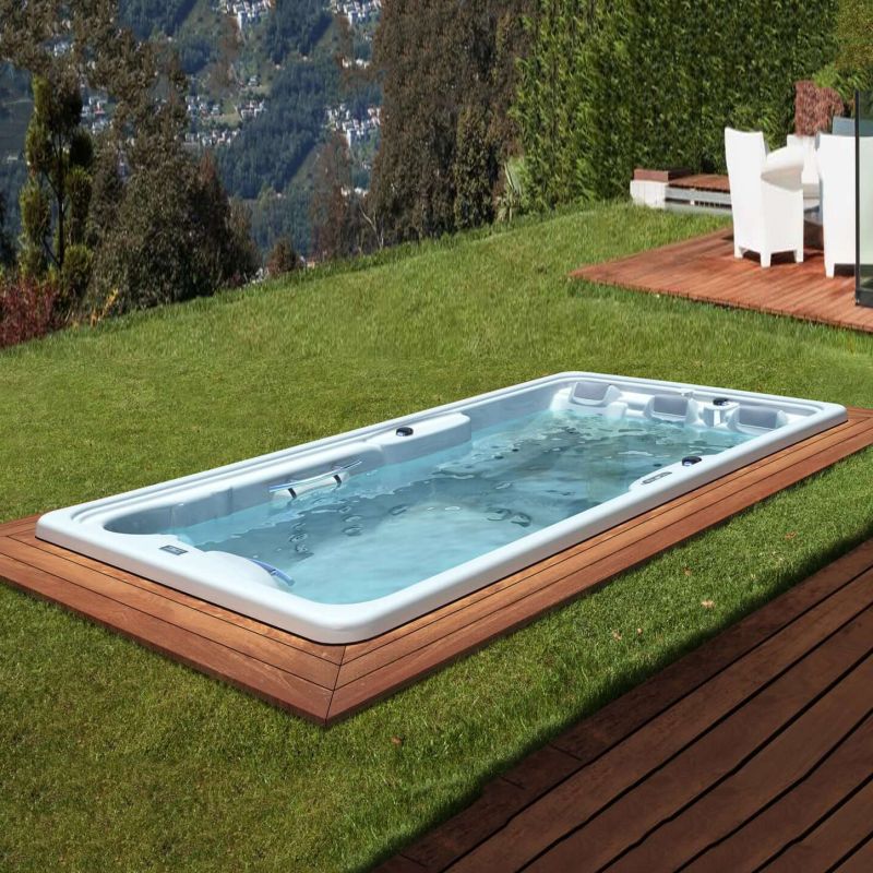 Vasca idromassaggio bianca con cornice in legno in un giardino verde con vista sulle montagne