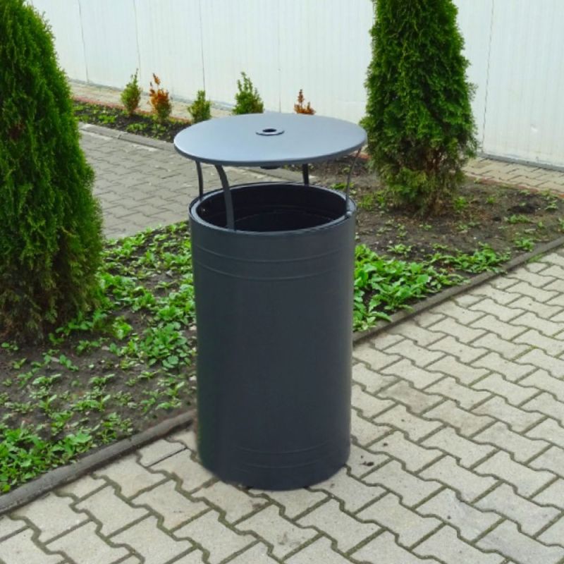 Bidone da giardino in metallo nero con coperchio a ribalta su sentiero accanto a piante verdi