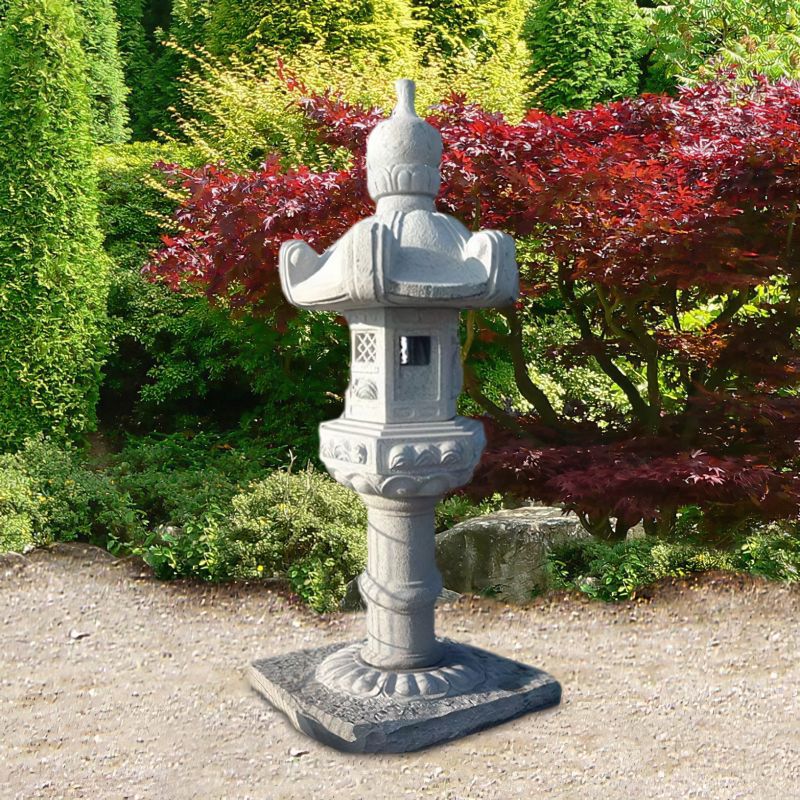 Lantern de jardin en pierre avec des arbustes et un érable rouge en arrière-plan