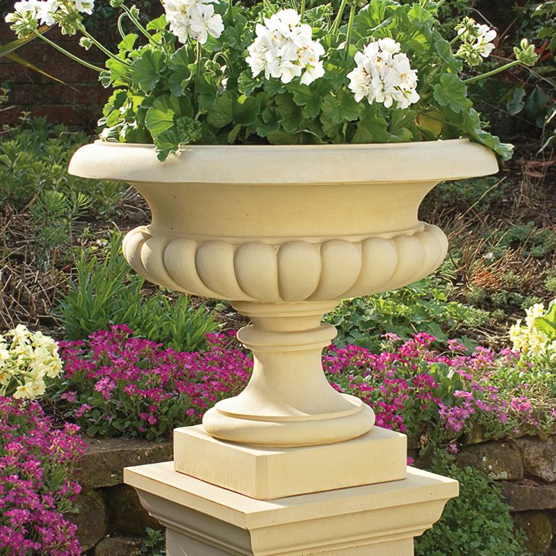 Pot de fleurs en pierre sur socle dans un jardin fleuri