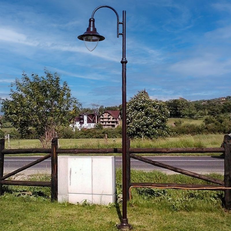 Lanterne de jardin antique sur un poteau noir fin avec pelouse verte et maison de campagne en arrière-plan