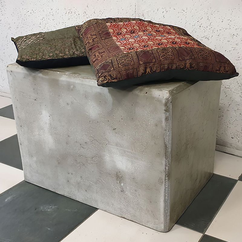 Sgabello robusto in cemento con cuscini decorativi su pavimento a scacchi bianco e nero