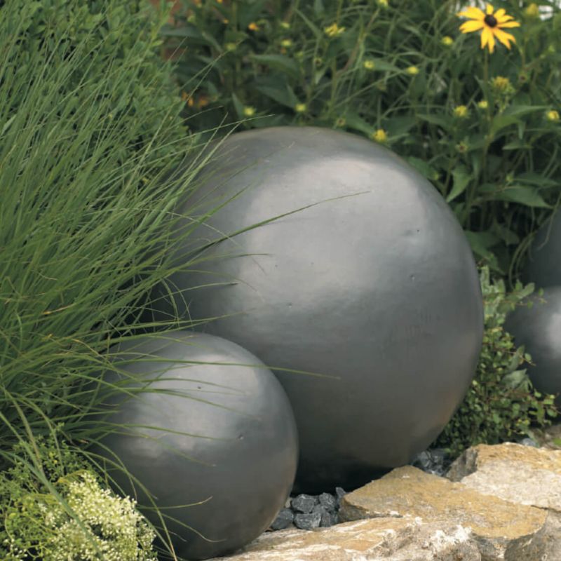 Deux boules décoratives de jardin grises en métal parmi des plantes et des pierres