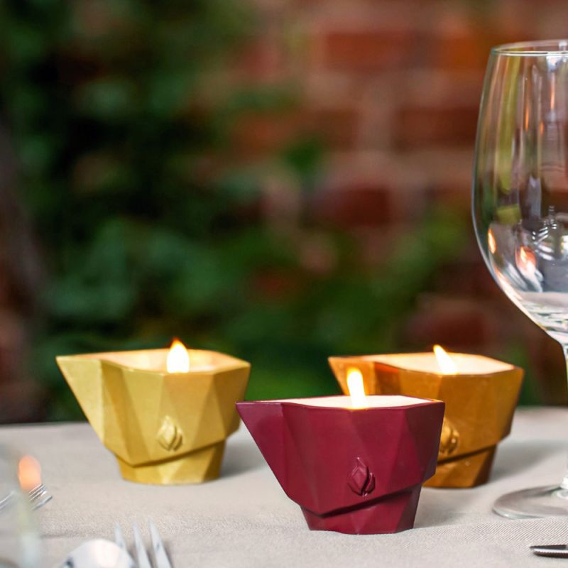 Tre candele da giardino accese in contenitori moderni su un tavolo da giardino con un bicchiere
