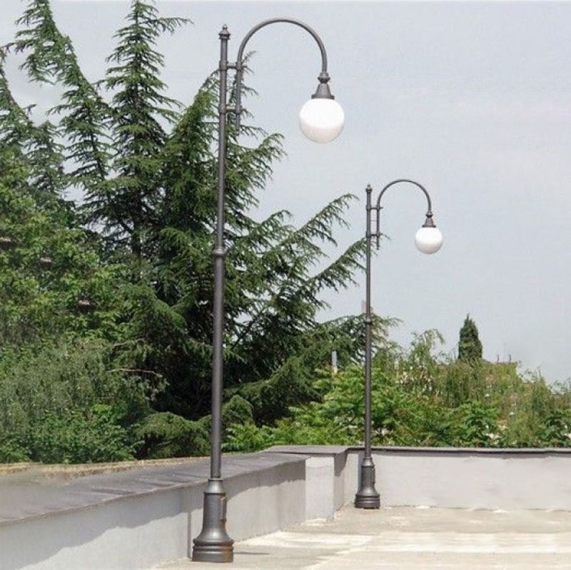 Deux lampadaires noirs avec des globes en verre blanc dans un espace extérieur avec des arbres en arrière-plan