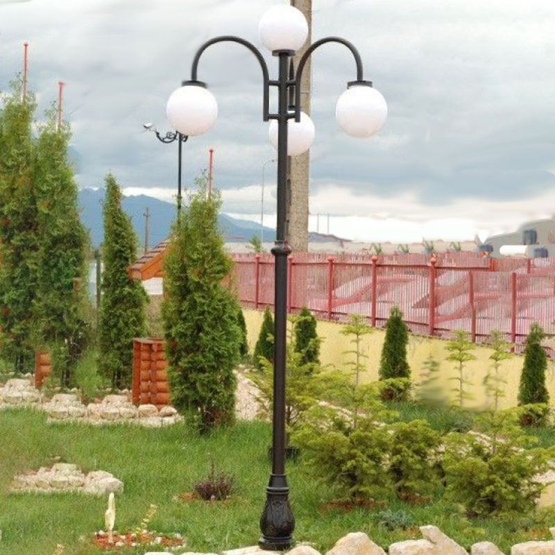 Lanterne de jardin noire avec quatre globes lumineux blancs entourée de plantes vertes et jardin en arrière-plan