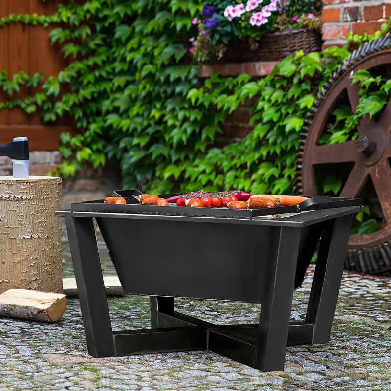 Barbecue quadrato nero con salsicce e carne davanti a un muro di mattoni e piante verdi