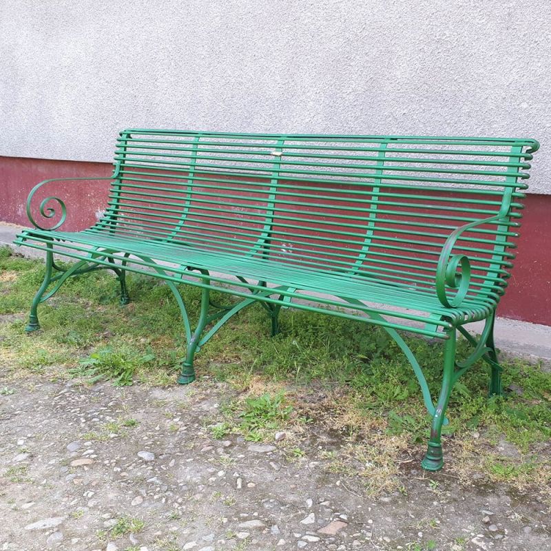 Banc de jardin en métal vert devant un mur rouge sur herbe et graviers