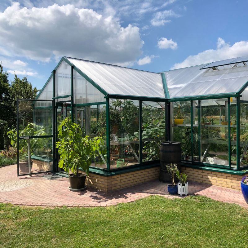 Serre verte en verre dans un jardin bien entretenu avec des plantes à l'intérieur