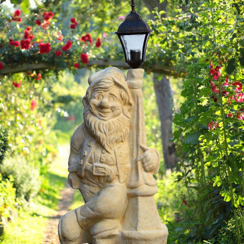 Nain de jardin en pierre avec lanterne entouré de fleurs et de verdure dans le jardin