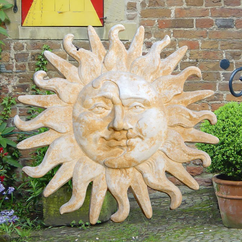 Scultura decorativa di sole con volto in pietra fissata a un muro di mattoni in un giardino