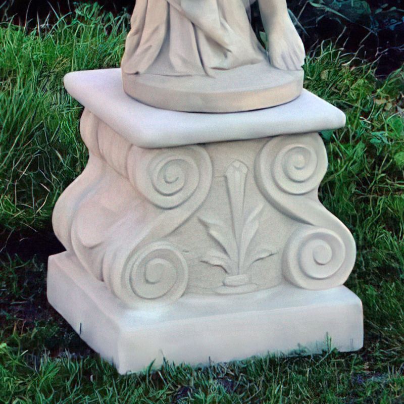 Socle en pierre fermé avec motifs décoratifs de feuilles et spirales, posé sur l'herbe dans un jardin