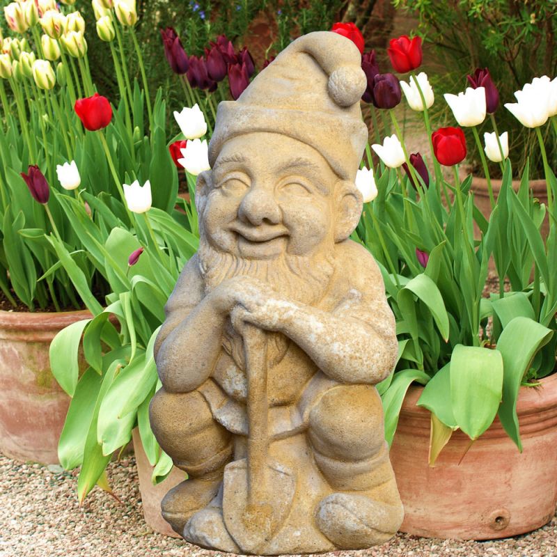 Steinerner Gartenzwerg hält Schaufel zwischen bunten Tulpen in Pflanztöpfen
