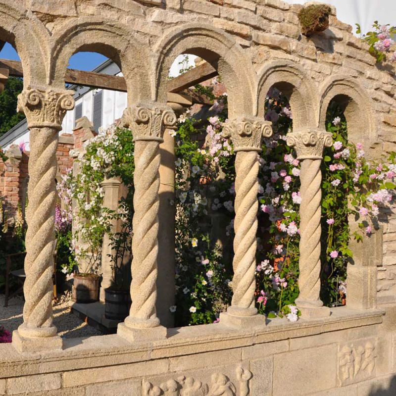 Architettura in pietra con colonne attorcigliate e rose rampicanti fiorite nel giardino