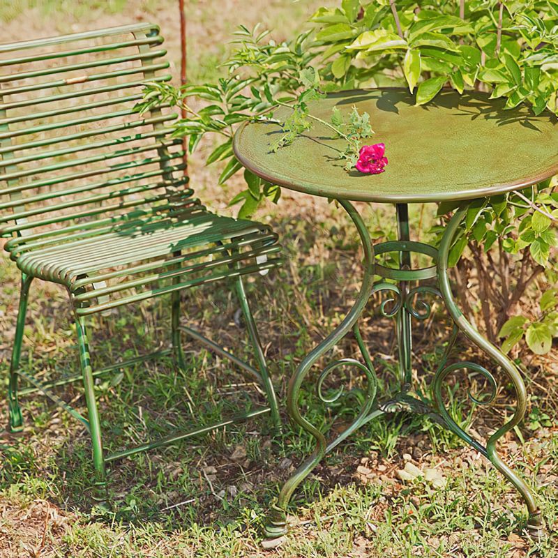 Tavolo in metallo verde con sedia abbinata in giardino con piante sullo sfondo