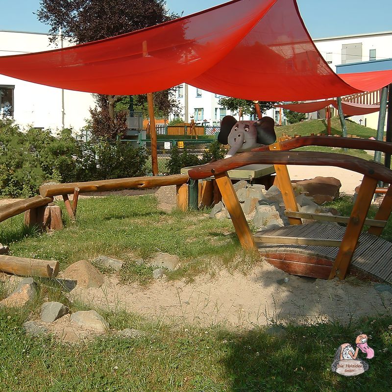 Tensostruttura rossa che offre ombra su un'area giochi per bambini con sabbiera e ponte in legno