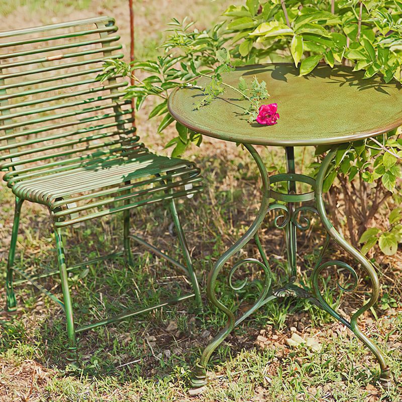 Table de jardin ronde en métal vert avec une fleur rouge dessus et chaise en métal vert dans le jardin