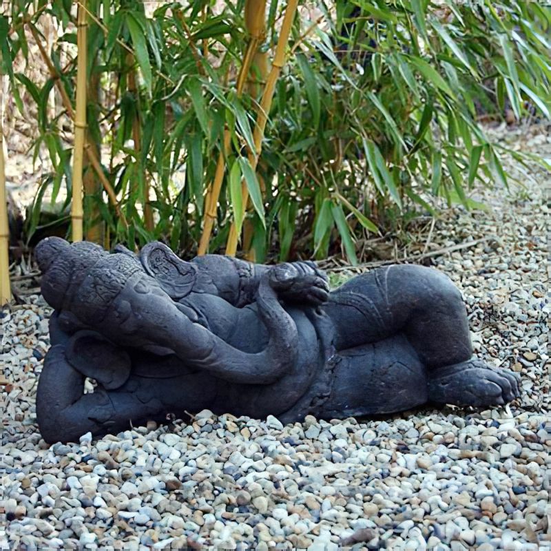 Sculpture sombre en forme d’éléphant couché sur des cailloux devant des plantes de bambou