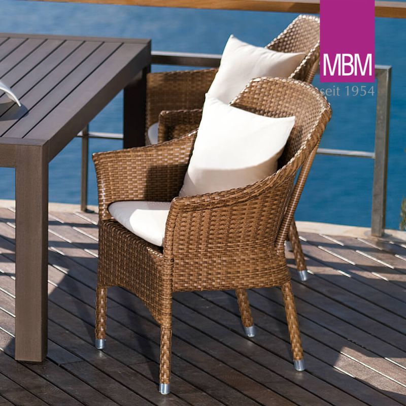 Chaise de jardin en rotin avec coussins blancs à côté d'une table en bois sur une terrasse au bord de l'eau