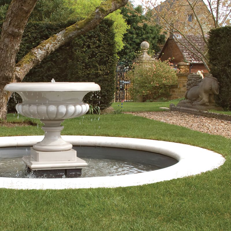 Fontana bianca in pietra con acqua corrente in un bel giardino con prato e casette da giardino