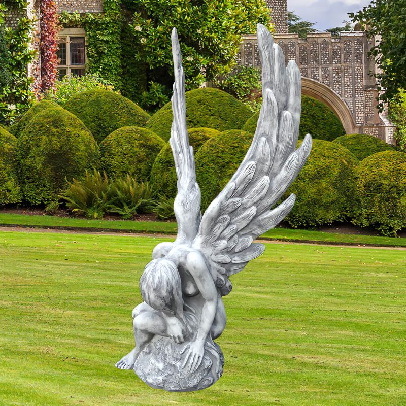 Figure d'ange blanche avec de grandes ailes déployées sur la pelouse devant une maison de jardin