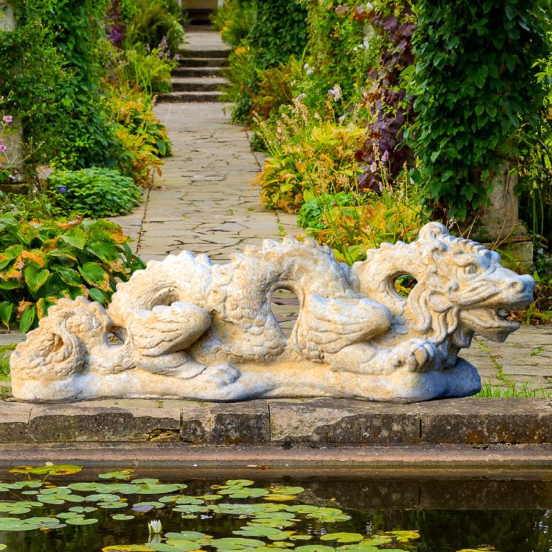 Scultura in pietra bianca di un drago sdraiato accanto a uno stagno nel giardino