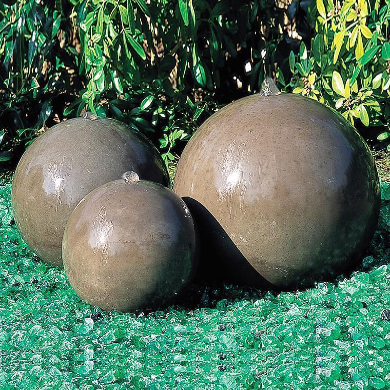 Trois grosses boules en pierre comme décoration de jardin sur pelouse verte devant des buissons