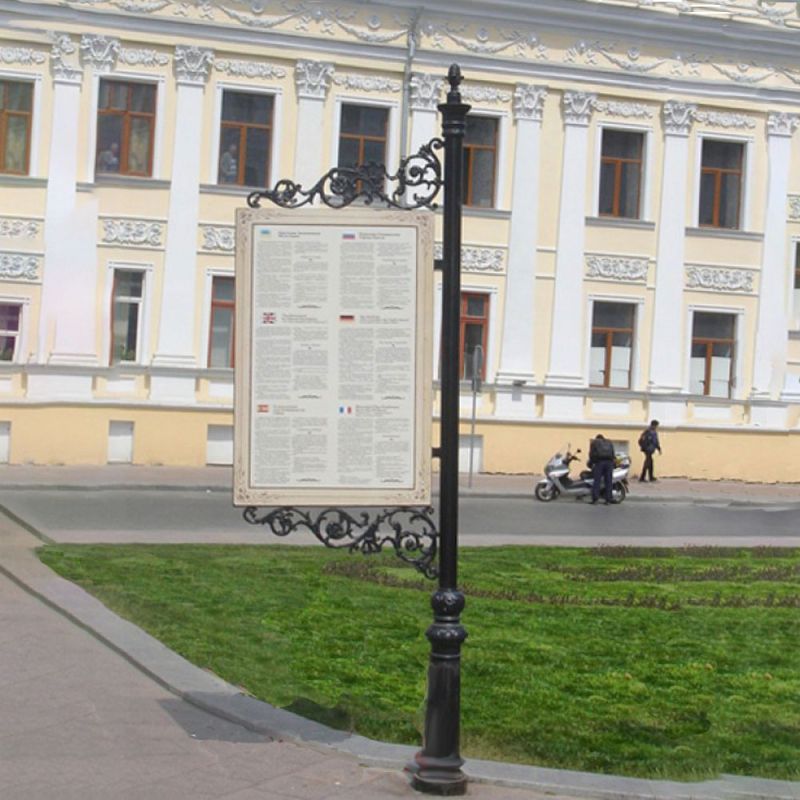 Un poteau d'affichage orné avec un panneau d'information devant un bâtiment historique et un espace vert