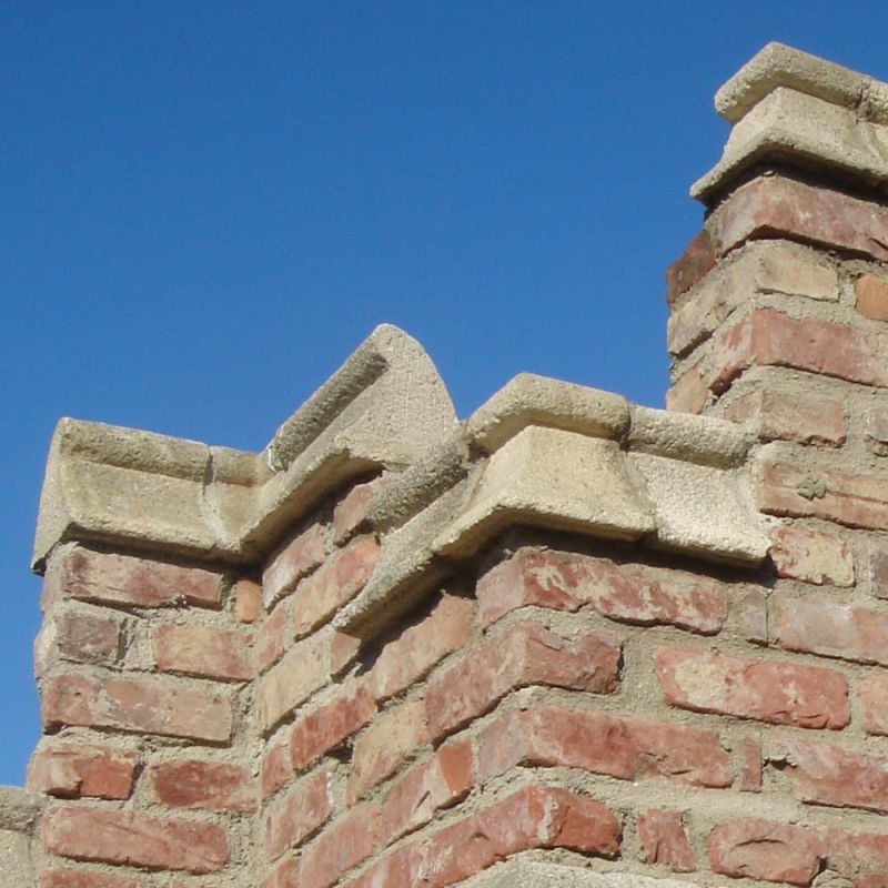 Gros plan sur un mur de briques rustique avec chapeaux de pierre décoratifs sous ciel bleu