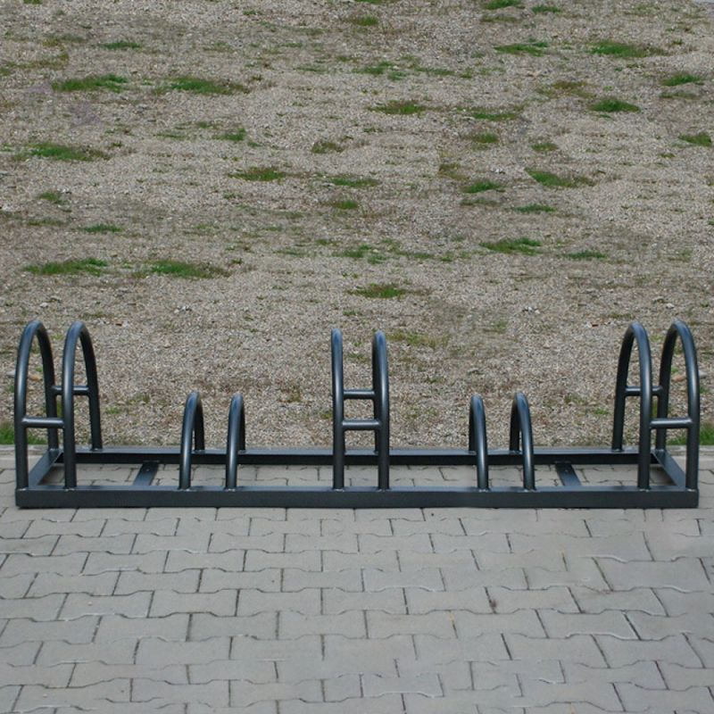 Support à vélos noir en métal sur sol pavé devant une pelouse