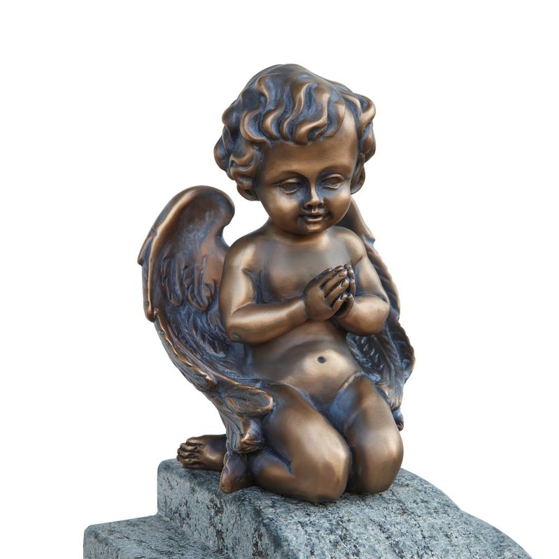Figure en bronze brun d'un ange agenouillé priant sur une pierre dans un jardin