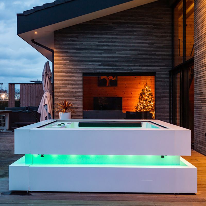 Douche de jardin blanche avec eau illuminée colorée sur une terrasse devant une maison moderne en soirée