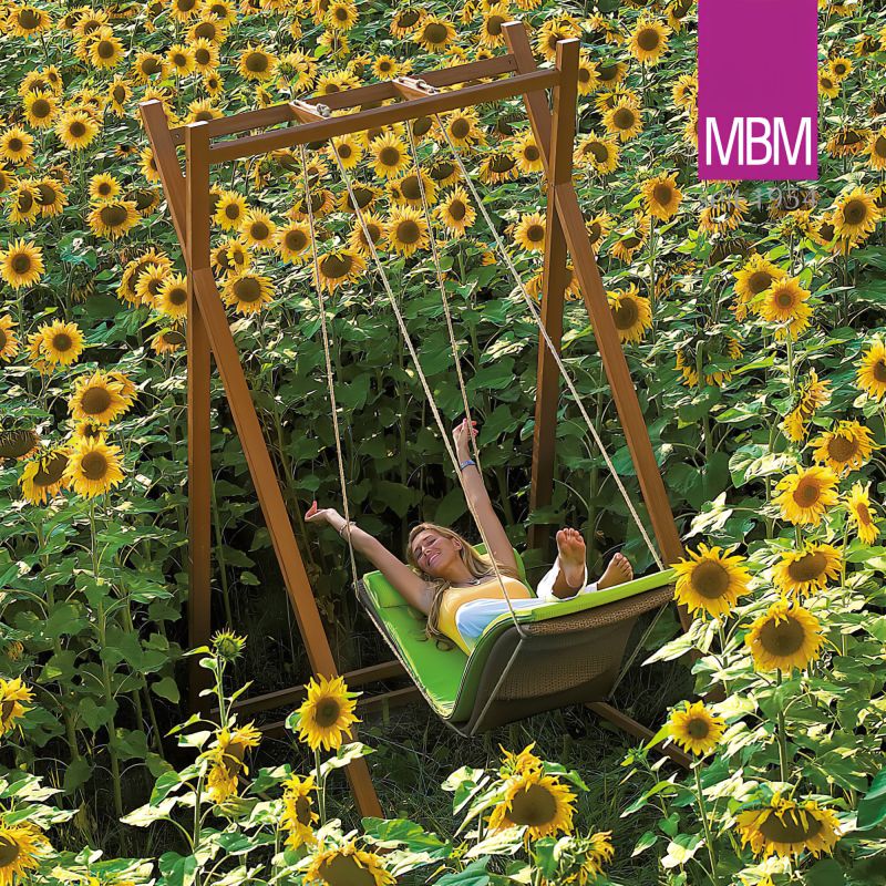Personne se détendant sur une chaise suspendue verte entourée de tournesols éclatants