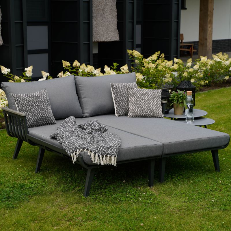 Canapé de jardin gris avec coussins et couverture sur pelouse verte