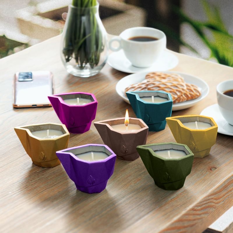 Sette candele da giardino di diversi colori su un tavolo di legno con una tazza di caffè e biscotti